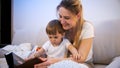 Portrait of smiling young mother with her toddler boy reading big old story book Royalty Free Stock Photo