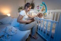 Portrait of young smiling mother in pajamas sitting on bed and reading book to her baby son before going to sleep Royalty Free Stock Photo