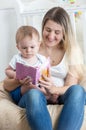 Portrait of smiling young mother sitting on beanbag with her baby boy and reading him book Royalty Free Stock Photo