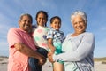 Portrait of smiling multiracial grandparents carrying grandchildren at beach against sky Royalty Free Stock Photo