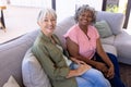 Portrait of smiling multiracial senior female friends sitting on sofa in living room at nursing home Royalty Free Stock Photo