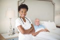 Portrait of smiling nurse standing with arms crossed while senior man lying on bed Royalty Free Stock Photo