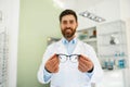 Portrait of ophthalmologist offering glasses to client in optics store