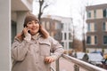 Portrait of smiling overweight woman in warm hat and jacket talking on mobile phone standing near railing at city street Royalty Free Stock Photo