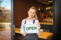 Portrait of smiling owner standing at restaurant door holding open sign, small family business