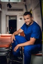 A portrait of a smiling paramedic in a uniform sitting in the back of an ambulance with a stretcher Royalty Free Stock Photo