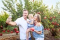 Portrait of smiling parents with baby girl daughter doing selfie photo with smart phone in the pomegrate fruit garden on the sunse