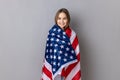 Patriotic little girl standing wrapped in american flag, looking at camera, relocating to America. Royalty Free Stock Photo