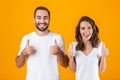 Portrait of smiling people man and woman in basic clothing showing thumbs up, while standing together isolated over yellow Royalty Free Stock Photo