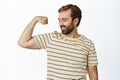 Portrait of smiling pleased man looking at his arm muscles, flexing biceps with satisfied face expression. Concept of