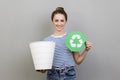 Woman holding green recycling sign and white bin for rubbish, looking at camera. Royalty Free Stock Photo