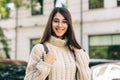 Portrait of smiling pretty girl looking at the camera, posing on the city street, wearing knitted sweater. Beautiful young woman Royalty Free Stock Photo