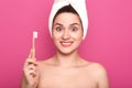 Portrait of smiling pretty woman with astonished facial expression, holds toothbrush over pink background and looking