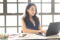 Portrait of smiling pretty young Asian business woman working on laptop in her workstation Royalty Free Stock Photo