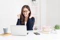 Portrait of smiling pretty young Asian businesswoman working on laptop and smiling while sitting at her desk in bright modern Royalty Free Stock Photo