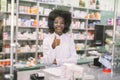 Portrait of smiling professional African female pharmacist in modern drugstore, standing behind the glass at the counter Royalty Free Stock Photo