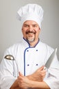 Portrait of a smiling professional chef cook man with a kitchen knife and a soup ladle, dressed a chef uniform, grey background Royalty Free Stock Photo