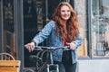 Portrait of smiling red curled long hair caucasian woman on the city street walking with a bicycle. Natural people beauty concept