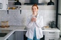 Portrait of smiling redhead woman holding cup of hot beverage in hands on morning at kitchen. Royalty Free Stock Photo