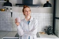 Portrait of smiling redhead woman holding cup of hot beverage in hands on morning at kitchen. Royalty Free Stock Photo