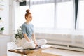 Portrait of smiling redhead young woman meditating while sits on desk at home office Royalty Free Stock Photo