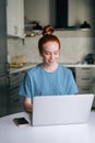 Portrait of smiling redhead young woman working typing on laptop computer sitting at table Royalty Free Stock Photo