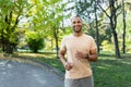 Portrait of smiling and satisfied african american man jogging in sunny park, man happy and looking at camera doing Royalty Free Stock Photo