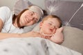 Portrait of smiling satisfied mother with her cute baby lying on bed in their morning, daughter sleeping, lying with closed eyes, Royalty Free Stock Photo