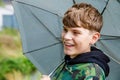 Portrait of a smiling school boy with rainbow umbrella in the park. Kid walking during rain. Happy positive child Royalty Free Stock Photo