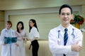 Portrait of smiling senior Asian male doctor in workwear with stethoscope, standing with arms crossed in clinic hospital, looks at Royalty Free Stock Photo