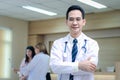 Portrait of smiling senior Asian male doctor in workwear with stethoscope, standing with arms crossed in clinic hospital, looks at Royalty Free Stock Photo