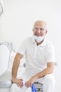 Portrait of smiling senior dentist sitting on chair at dental clinic