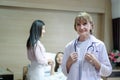 Portrait of smiling senior female doctor in workwear with stethoscope standing in recovery room at clinic hospital with patient Royalty Free Stock Photo