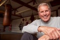 Portrait Of Smiling Senior Male Boxing Coach In Gym Standing By Old Fashioned Leather Punching Bags Royalty Free Stock Photo