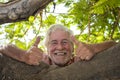 Portrait of smiling senior man leaning against the branches of a plant in the park in the shade gesturing ok with hands - concept