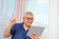 Portrait of smiling senior man reading news on digital tablet. Cheerful excited mature male using portable computer at home Royalty Free Stock Photo