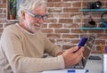 Portrait of smiling senior man using mobile phone and laptop computer at home . Brick wall on background Royalty Free Stock Photo