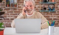 Portrait of smiling senior man using mobile phone and laptop computer at home . Brick wall on background Royalty Free Stock Photo