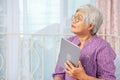 Portrait of smiling senior woman with eyeglasses thinking while looking up using electronic tablet while relaxing at the bed room Royalty Free Stock Photo