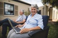 Portrait of smiling senior woman holding laptop on couch in backyard Royalty Free Stock Photo