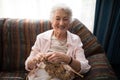 Portrait of smiling senior woman knitting while sitting on sofa against window