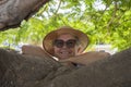 Portrait of smiling senior woman in the shade of a plant in the park with arms resting on branches - active retired seniors and