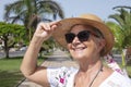 Portrait of a smiling senior woman with a straw hat and sunglasses standing in a public park Royalty Free Stock Photo