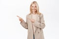 Portrait of smiling senior woman, 50 years old lady in trench coat, pointing finger left, looking happy and healthy Royalty Free Stock Photo