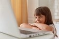 Portrait of smiling small dark haired female child sitting at table in front of laptop computer and smiling, little preschooler Royalty Free Stock Photo