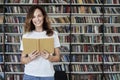 Portrait of smiling smart woman model reading with opened book in a library, bookshelf behind, long hair. Hipster college student Royalty Free Stock Photo