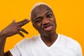 Portrait of a smiling smiling charismatic african man in a white t-shirt holding his fingers near his temple on a yellow