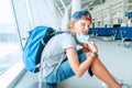 Portrait of smiling solo traveler boy with a backpack in empty airport passenger transfer hall take off protective face mask and Royalty Free Stock Photo