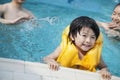 Portrait of smiling son in the water and holding onto the pools edge with family in the background Royalty Free Stock Photo