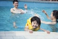 Portrait of smiling son in the water and holding onto the pools edge with family in the background Royalty Free Stock Photo